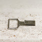 Die Niwaki 'Belt Clip' Praktische Halterung für Niwaki Single Holster, ein Metallclip mit einem rechteckigen Karabiner und kleinen quadratisch angeordneten Löchern, ruht auf strukturiertem hellem Stein - perfekt als Gartenschere Halterung oder Gürtelbefestigung.