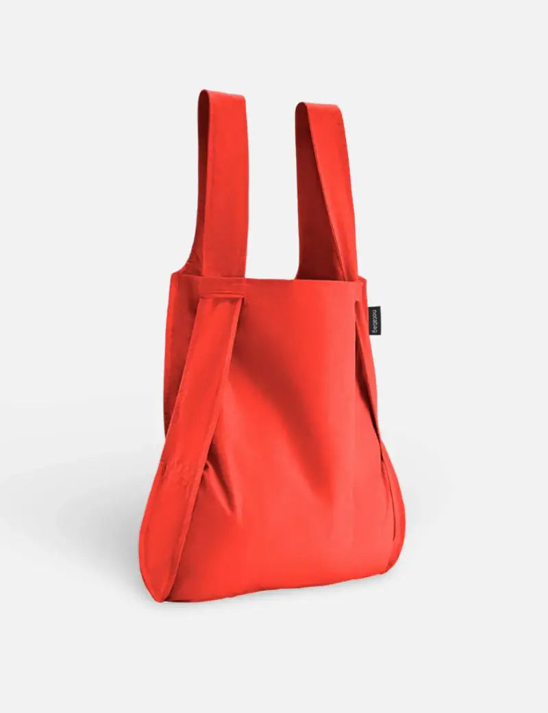 Der Notabag | „Original Red“ – Tasche und Rucksack in einem von Notabag, eine leuchtend rote Mehrwegtasche mit breiten Tragegriffen, steht aufrecht vor einem schlichten weißen Hintergrund.