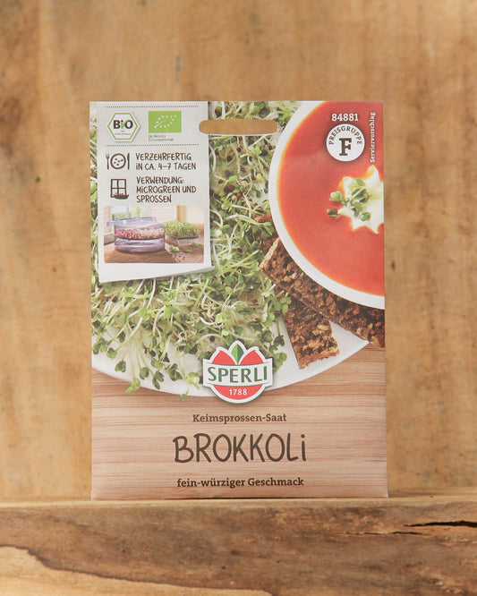 Päckchen mit Sperli's Bio Keimsprossen Saatgut 'Brokkoli' mit Abbildungen von frischen Sprossen, Knäckebrot und Tomatensuppe. Der deutsche Text hebt die Bio-Zertifizierung hervor und gibt Anleitungen für die Keimung von Brokkoli Sprossen.