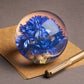 Der Hafod Grange | Briefbeschwerer mit Kornblume von Hafod Grange mit leuchtend blauen Kornblumen in klarem Glas sitzt auf braunem Papier mit einem goldenen Stift - ein elegantes Schreibtisch-Accessoire für Ihren Schreibtisch.