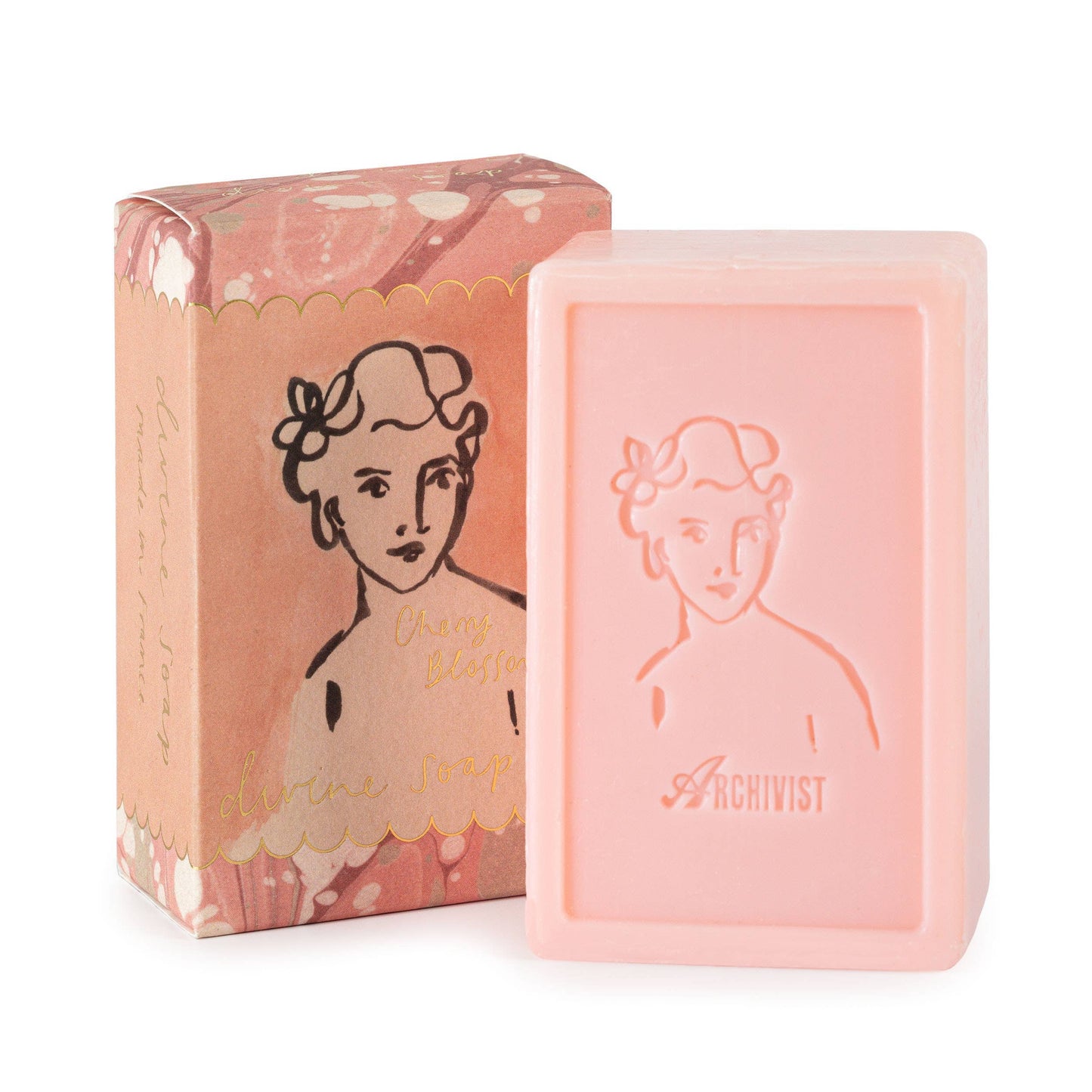 Ein rosafarbener Riegel Archivist Gallery 'Cherry Blossom' Handseife 150 g mit geprägtem Frauengesicht, daneben die blumengeschmückte roségoldene Schachtel - ideal für luxuriöse Körperpflege.