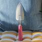 Eine handgefertigte Metall-Schaufel 'Pink Tulip' von Chop Chop Bloom mit pinkem Griff steht auf einem gelb-weiß gestreiften Kissen vor einem blau-weiß gestreiften Polster, "Made in Germany" ist auf der Klinge eingraviert.