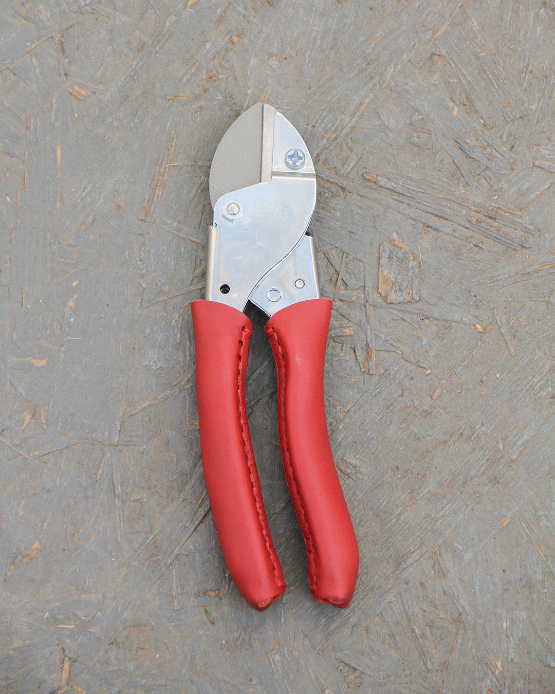 Die Chop Chop | Exklusive rote Gartenschere 'Chili Pepper' von Chop Chop Bloom mit Metallklinge ruht auf einer strukturierten grauen Holzoberfläche - bereit für Ihre nächste Schnittaufgabe.