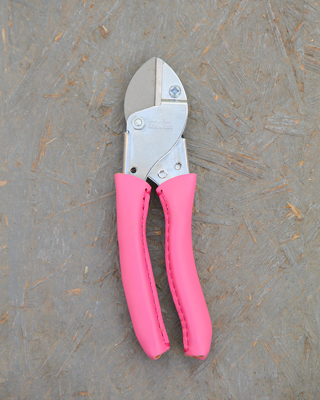 Ein Paar Chop Chop | Hochwertige Gartenschere 'Pink Tulip' von Chop Chop Bloom mit leuchtend rosa Griffen, die die Initiative Brustkrebs unterstützen, ruht auf einer strukturierten graubraunen Oberfläche.