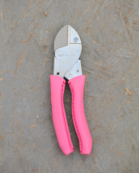 Ein Paar Chop Chop | Hochwertige Gartenschere 'Pink Tulip' von Chop Chop Bloom mit leuchtend rosa Griffen, die die Initiative Brustkrebs unterstützen, ruht auf einer strukturierten graubraunen Oberfläche.