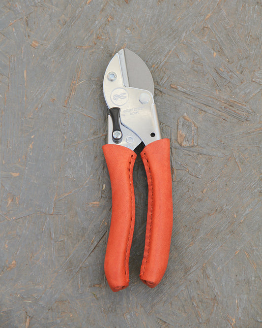 Ein Paar Chop Chop | Hochwertige Gartenschere 'Tiger Lilly' von Chop Chop Bloom mit orangefarbenen, strukturierten Stielen auf einer grauen, rauen Holzoberfläche - ideal für alle, die Wert auf Präzision in ihrem Tiger Lilly Garten legen.