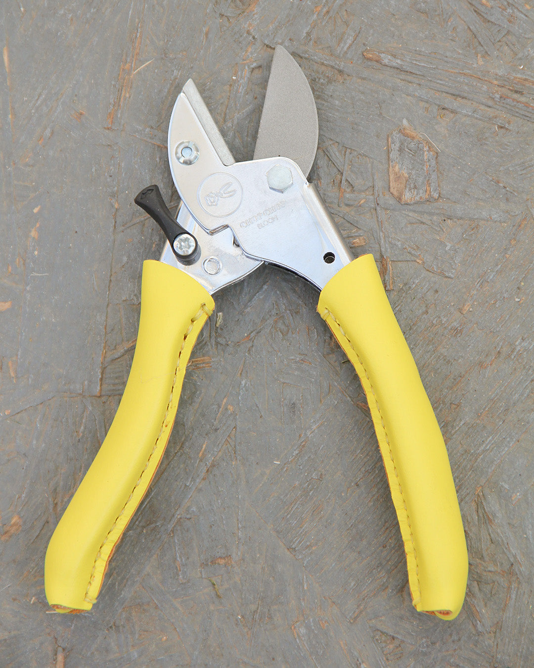 Ein Paar Chop Chop | Hochwertige Gartenschere 'Busy Lizzy' von Chop Chop Bloom mit einer Metallklinge und leuchtend gelben Griffen ruht auf einer strukturierten grauen Holzoberfläche.