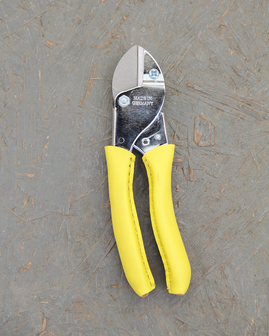 Ein Paar Metalldrahtschneider "Busy Lizzy" von Chop Chop Bloom mit gelben Griffen liegt auf einer strukturierten grauen Oberfläche.