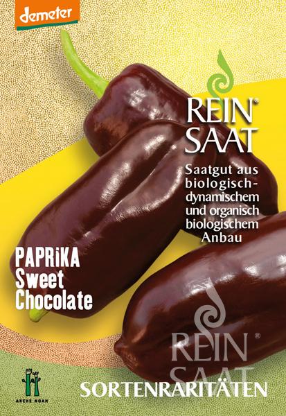 Eine Saatgutpackung von Reinsaat für Paprika 'Sweet Chocolate' (Capsicum annuum) mit drei dunkelvioletten Paprikaschoten, mit deutschem Text über biologischen und biodynamischen Anbau, mit der Aufschrift samenfest und der Marke Reinsaat.