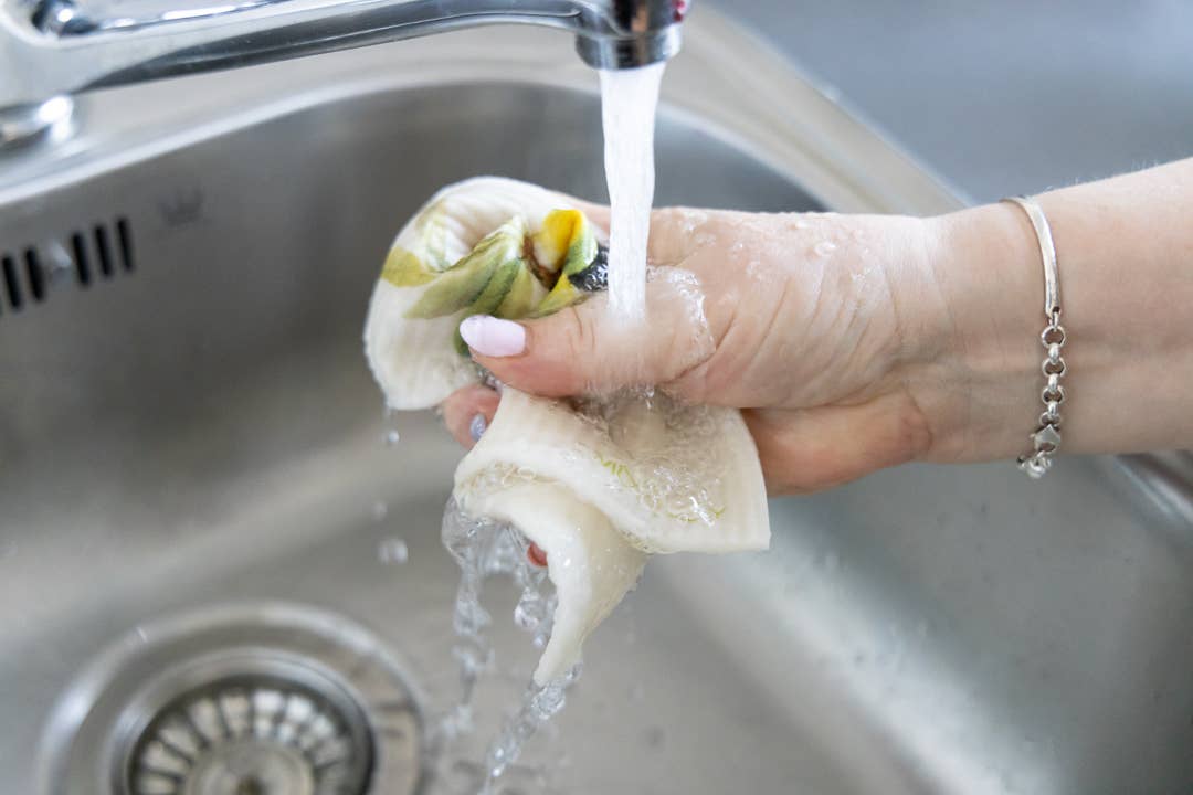 Eine Hand spült einen frisch gepflückten Pilz unter fließendem Leitungswasser in einer Küchenspüle ab, wobei Wassertropfen sichtbar sind und ein More Joy | 'Tomaten' Biologisch abbaubares Schwammtuch von More Joy Home in der Nähe ist.