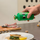 Eine Hand gießt Yiayia and friends | Natives Olivenöl extra mit Basilikum 200 ml über Fisch und Spinat auf einen Teller mit einer Zitronenspalte. Im Hintergrund stehen frischer Fisch, Zitrone und Feinkost-Zutaten von yiayia and friends auf dem Tresen.