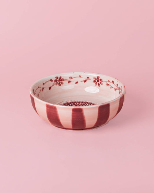 Wir präsentieren: Alfar Tierra Cocida | Keramikschale mit Knoblauchreibe, Mittelrosa „Sakura“ – eine wunderschöne, handbemalte spanische Keramikschale von Alfar Tierra Cocida. Mit roten Streifen auf der Außenseite und einem zarten Blumenmuster auf der Innenseite, alles vor einem bezaubernden rosa Hintergrund, bringt dieser reizvolle Küchenhelfer authentisches mediterranes Flair in Ihre Küche.