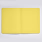 Ein nuuna „Not White Yellow“ L Light A5+ Notizbuch-Set mit Gelstift und leeren, gelben Seiten liegt offen auf einer hellgrauen Unterlage.