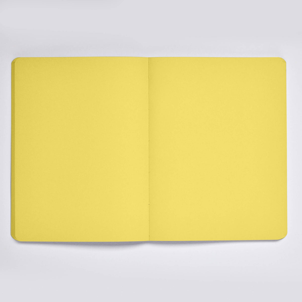 Ein nuuna „Not White Yellow“ L Light A5+ Notizbuch-Set mit Gelstift und leeren, gelben Seiten liegt offen auf einer hellgrauen Unterlage.