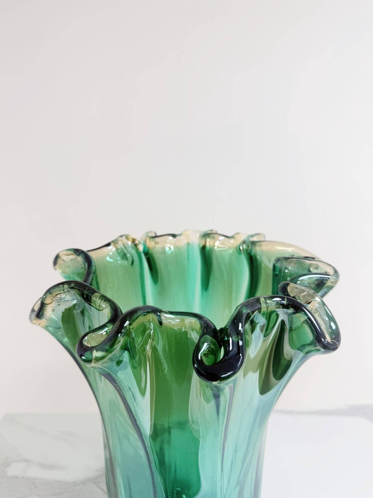 Die Murano Dream | Große „Fazzoletto“-Vase aus grünem Murano-Glas (H 32, Ø 24 cm) besticht durch ihren gewellten Rand und ihr fließendes Design. Sie steht auf hellem Untergrund vor einem schlichten Hintergrund.