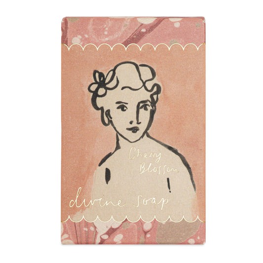 Ein 150 g schwerer rechteckiger Riegel Archivist Gallery | 'Cherry Blossom' Handseife ist in einer rosafarbenen Verpackung mit einer illustrierten Frau und weißen Wellenkanten verpackt, perfekt für luxuriöse Körperpflege.