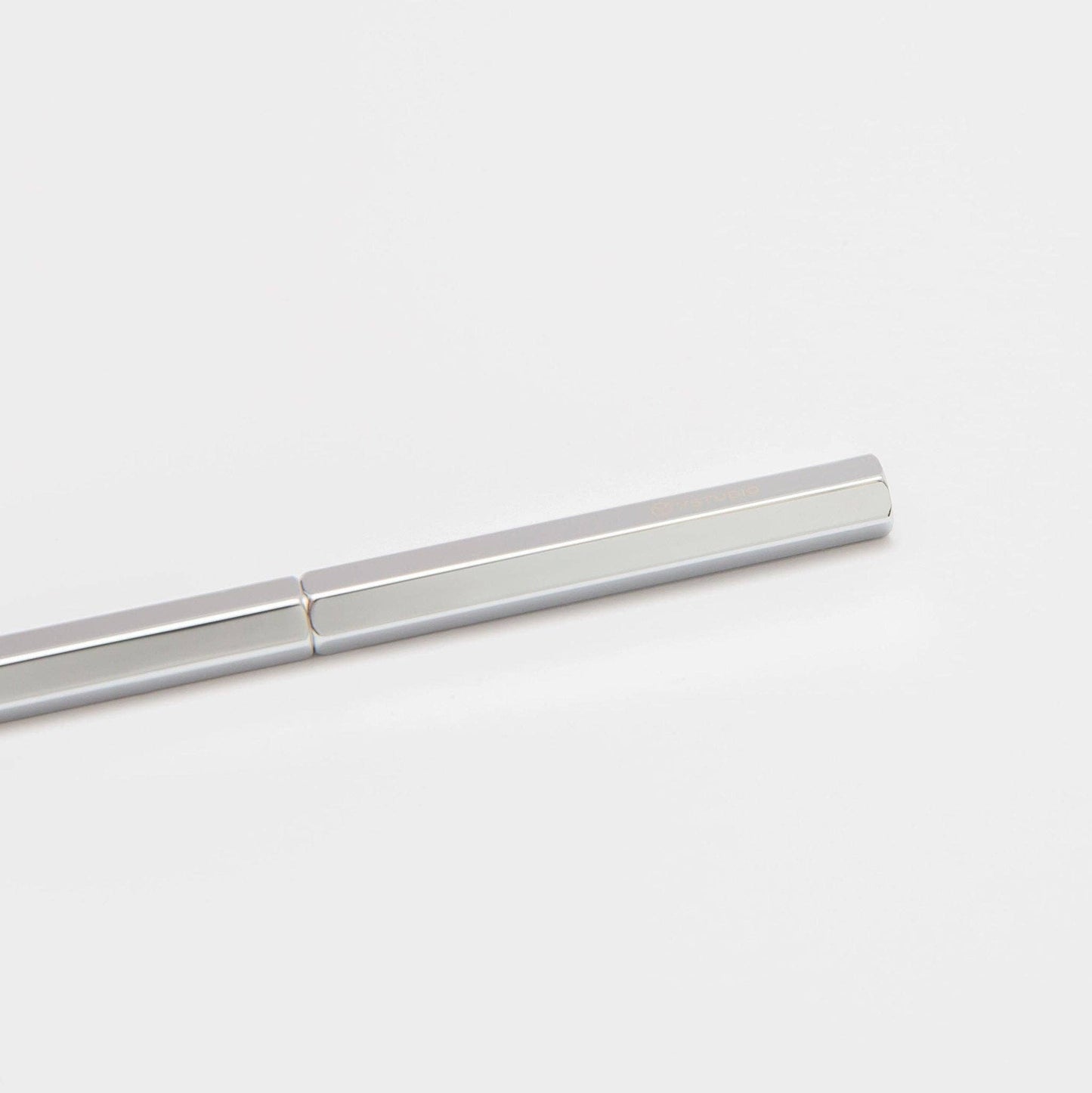 Ein minimalistisches Bild des ENTREPÔT YSTUDIO Klassischer Revolve Kugelschreiber Slim (Glänzendes Silber), ein schlanker, sechseckiger silberner Kugelschreiber, der diagonal auf einem schlichten weißen Hintergrund platziert ist und in seiner Mitte ein subtiles Gelenk aufweist.