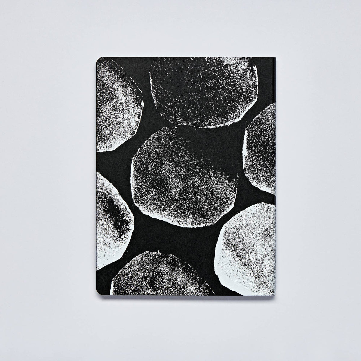 Ein nuuna | „Genesis“-Notizbuch „Not Ordinary L Light“ im Format A5+, mit schwarzem Einband und einem auffälligen weißen, abstrakten, kreisförmigen Punktraster-Muster, das an strukturierte Drucke erinnert – Notizbuchseiten aus hochwertigem Papier von nuuna.