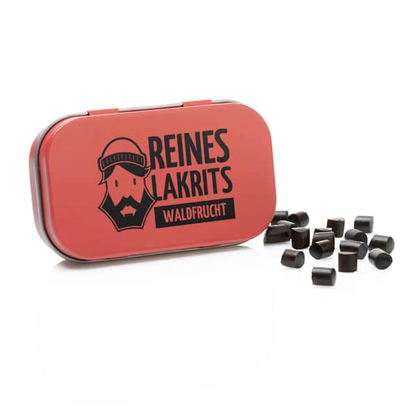 Eine geöffnete rote LASSE LAKRITS-Dose mit der Aufschrift "Dose Reines Lakritz Waldfrucht" mit einem bärtigen Cartoon-Gesicht zeigt schwarze, zuckerfreie Lakritz-Bonbons, die daneben auf weißem Hintergrund verstreut sind.