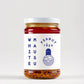 Ein Klarglasgefäß mit weißem Deckel enthält stückiges, rotes Umami-Chili-Öl. Auf dem Etikett steht in blauer Schrift "White Mausu | Erdnuss Rayu Sauce 440 g" von White Mausu Ltd. mit einer minimalistischen Vogelillustration.