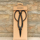 Schwarze Barebones | Artisan Gartenschere aus Edelstahl in einer minimalistischen Verpackung mit der Aufschrift Barebones; unten steht Artisan Pruning Shears" vor einem Hintergrund aus strukturiertem Stein.