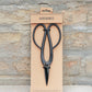 Schwarze Metall-Gartenscheren mit großen Griffen werden in einer minimalistischen braunen Verpackung mit der Aufschrift „Barebones“ und „Artisan Gartenschere aus Edelstahl“ vor einem strukturierten Steinhintergrund präsentiert – diese Barebones-Scheren verbinden elegantes Design mit professioneller Funktionalität.