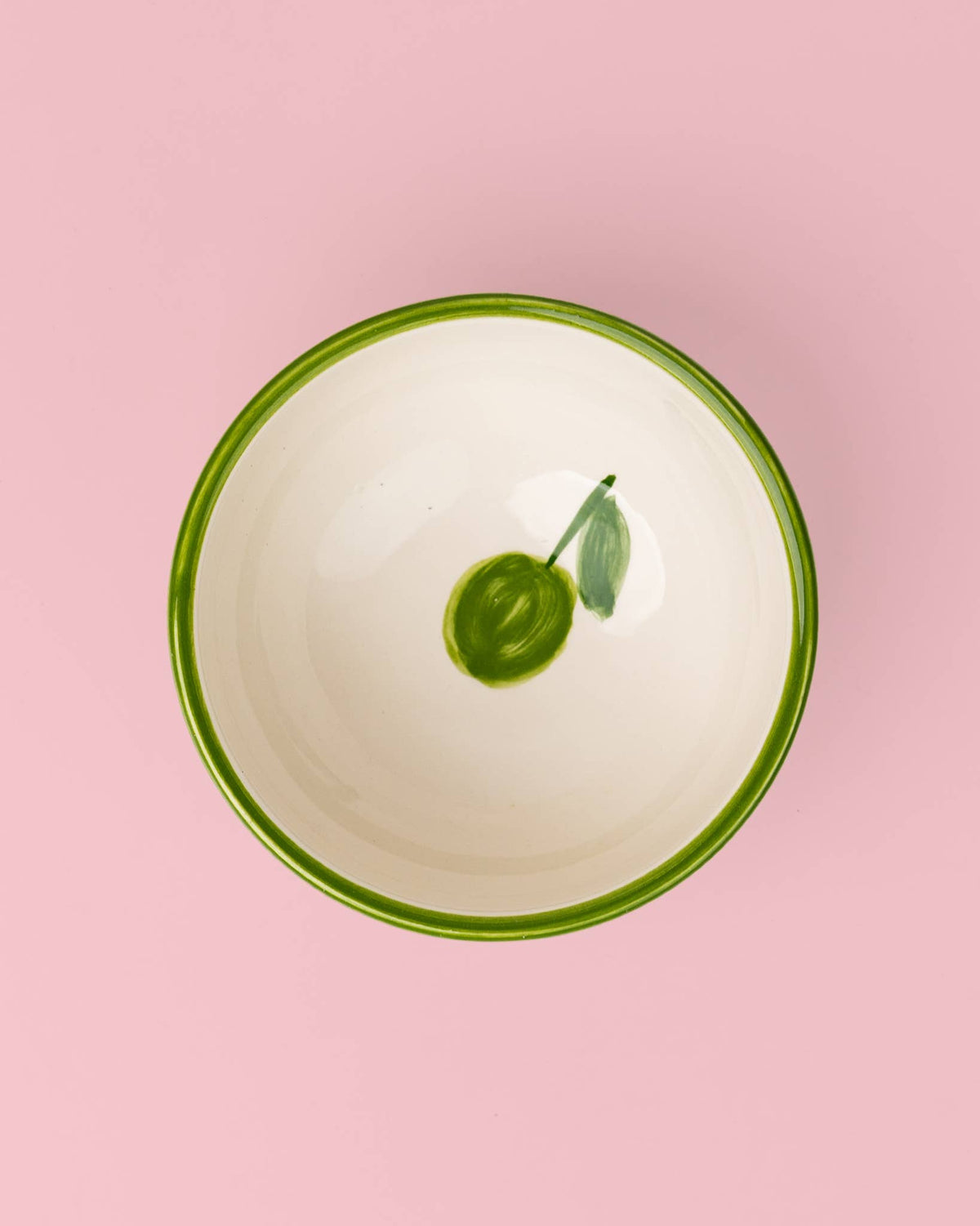 Die handgefertigte kleine Keramikschale „Olive“ von Alfar Tierra Cocida ist weiß, hat einen grünen Rand und ist innen mit einem handgemalten grünen Olivenzweig verziert. Inspiriert von mediterraner Keramik und in Spanien hergestellt, wird sie vor einem kräftigen rosa Hintergrund präsentiert.