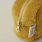 Nahaufnahme der Sylvie Thiriez Kosmetiktasche Honigfarben aus Plüsch mit goldenem Reißverschluss und weißem Seitenetikett. Diese weiche Tasche von Sylvie Thiriez ist OEKO-TEX zertifiziert und liegt auf einer leichten Oberfläche.