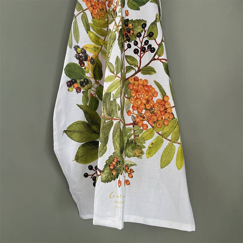 Das Geschirrtuch von Koustrupco aus 100 % Bio-Baumwolle mit Herbstmotiv besticht durch einen weißen Hintergrund, der mit einem botanischen Muster aus grünen Blättern und Trauben aus orangefarbenen und dunkelvioletten Beeren verziert ist, die sich vor einem gedeckten grünen Hintergrund abheben.