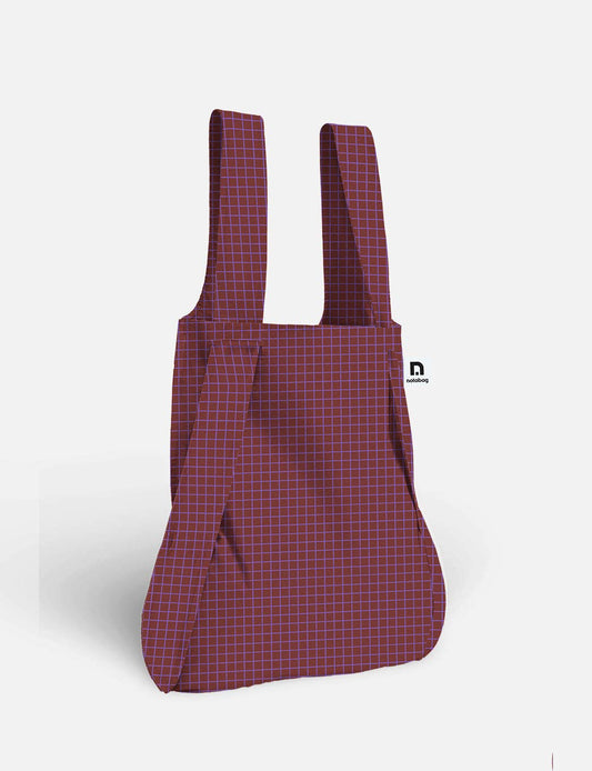 Eine Notabag | Die wandelbare Tasche und der Rucksack „Pflaume“ von Notabag mit rot-blauem Karomuster, zwei breiten Tragegriffen und einem seitlichen Riemen werden vor einem schlichten weißen Hintergrund präsentiert.