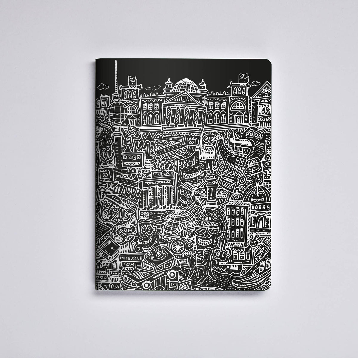 Ein nuuna „Berlin“-Notizbuch Graphic L im Format A5+, dessen schwarzer Einband aus recyceltem Leder mit einer detailreichen weißen Illustration der Berliner Stadtlandschaft mit Gebäuden und Sehenswürdigkeiten verziert ist, wird vor einem schlichten weißen Hintergrund präsentiert.