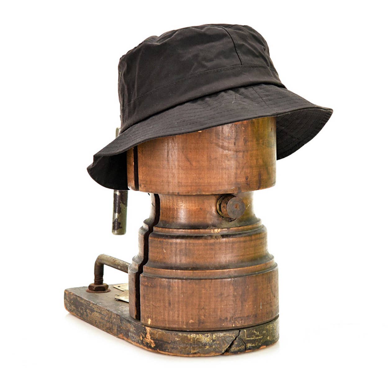 Ein Wachstropfen Krempenhut von Tweedmill Textiles, aus schwarzer gewachster Baumwolle mit breiter Krempe, sitzt auf einem alten Holzhutblock vor einem schlichten weißen Hintergrund.