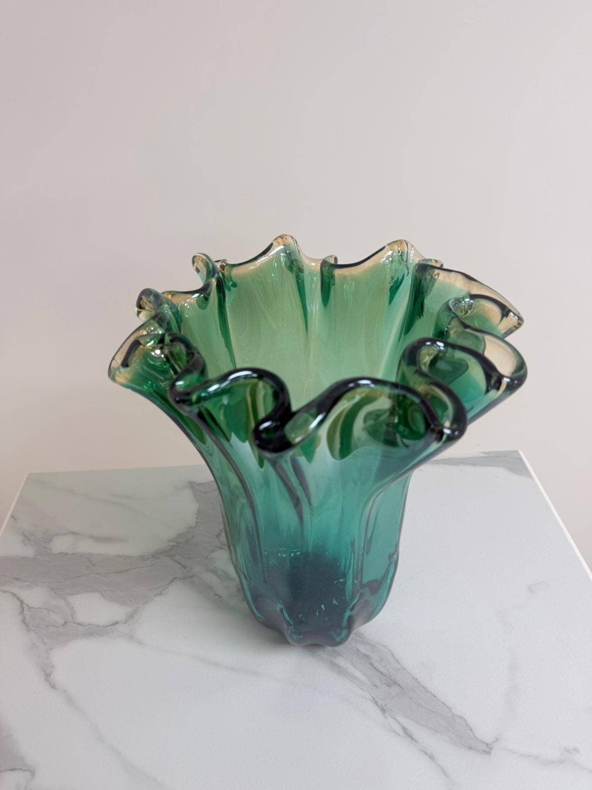 Die „Murano Dream Große ‚Fazzoletto‘“-Vase aus grünem Murano-Glas (H 32, Ø 24 cm) mit gewelltem Rand steht auf einer weißen Marmorplatte vor hellem Hintergrund.
