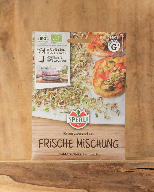 Eine Packung Sperli's | Bio Keimsprossen Saatgut 'Frische Mischung' ist auf Holz ausgestellt und zeigt frische Sprossen und Mahlzeiten. Die Verpackung hebt die Bio-Saatgut-Zertifizierung und eine schnelle Keimzeit hervor.