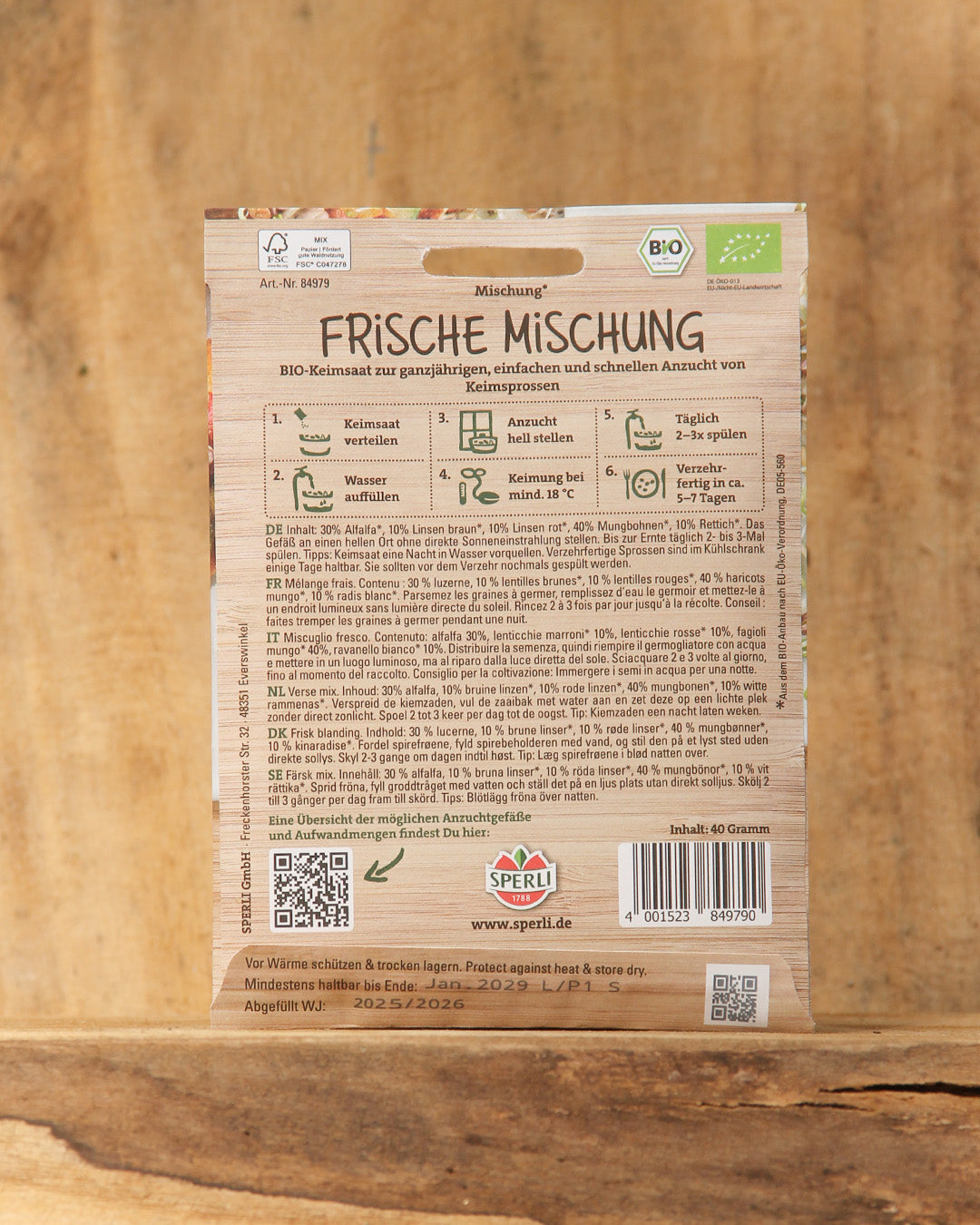 Eine Packung Sperli's Bio Keimsprossen Saatgut 'Frische Mischung' enthält auf der Verpackung vor einem Holzhintergrund eine ausführliche Pflanzanleitung, eine Produktinformation in deutscher Sprache, einen Strichcode, Icons und die Kontaktdaten des Unternehmens.