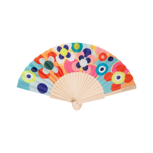 Der Handfächer „Sushi“ von Remember verfügt über Holzstreben und einen farbenfrohen Stoff, der mit auffälligen, abstrakten Blumen- und Kreismotiven in Blau, Gelb, Rot, Orange, Rosa und Grün verziert ist – damit ist dieses stilvolle Accessoire der perfekte Sommerbegleiter für luftige Eleganz an warmen Tagen.