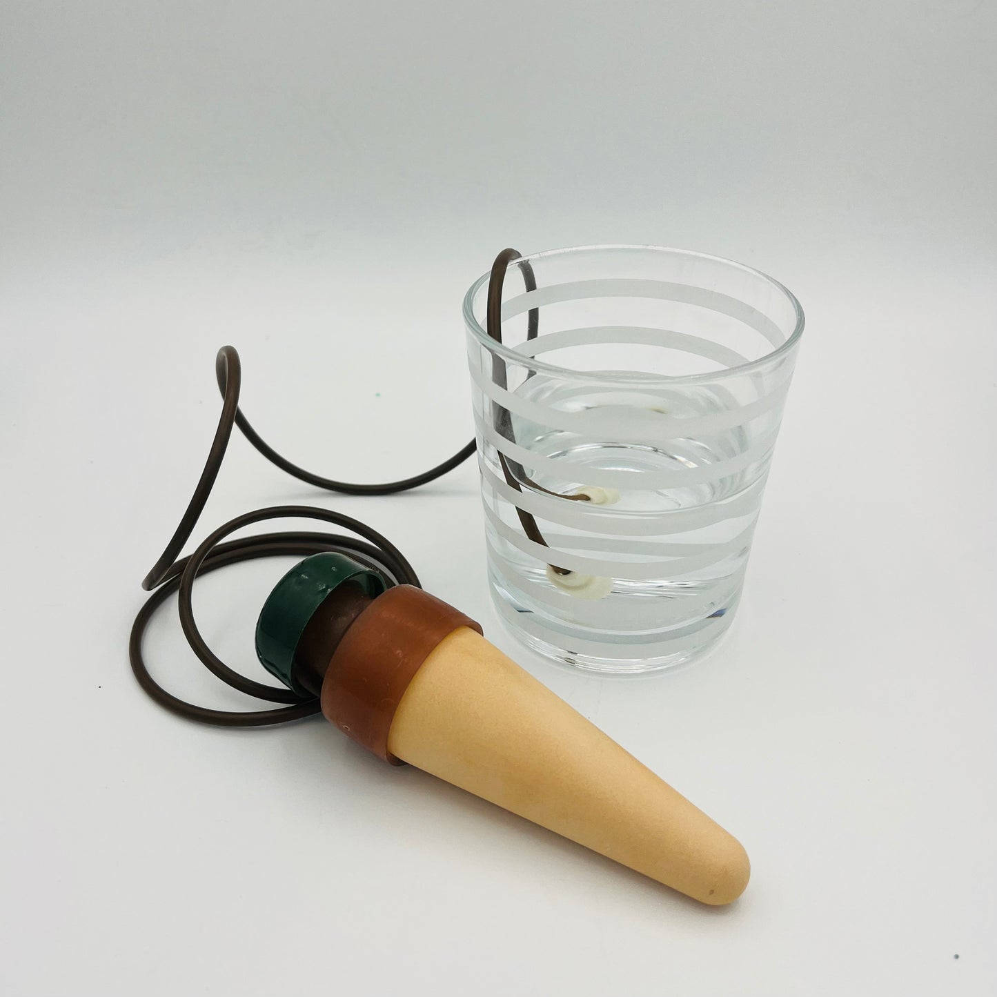 Zwei selbstbewässernde Pflanzenspieße Blumat Classic XL von Blumat, jeweils mit Keramikkegel und braunem Rohr, sind auf weißem Hintergrund neben einem klaren Wasserglas abgebildet. Ein gewundenes Rohr ist mit seinem Ende zur Pflanzenbewässerung im Wasser eingetaucht.