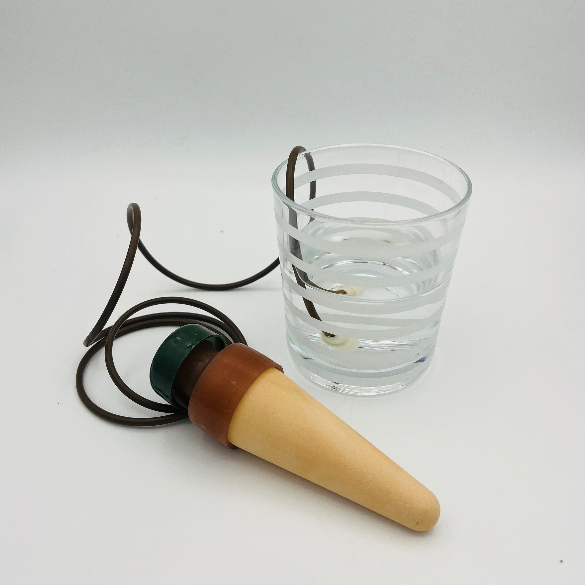 Zwei selbstbewässernde Pflanzenspieße Blumat Classic XL von Blumat, jeweils mit Keramikkegel und braunem Rohr, sind auf weißem Hintergrund neben einem klaren Wasserglas abgebildet. Ein gewundenes Rohr ist mit seinem Ende zur Pflanzenbewässerung im Wasser eingetaucht.