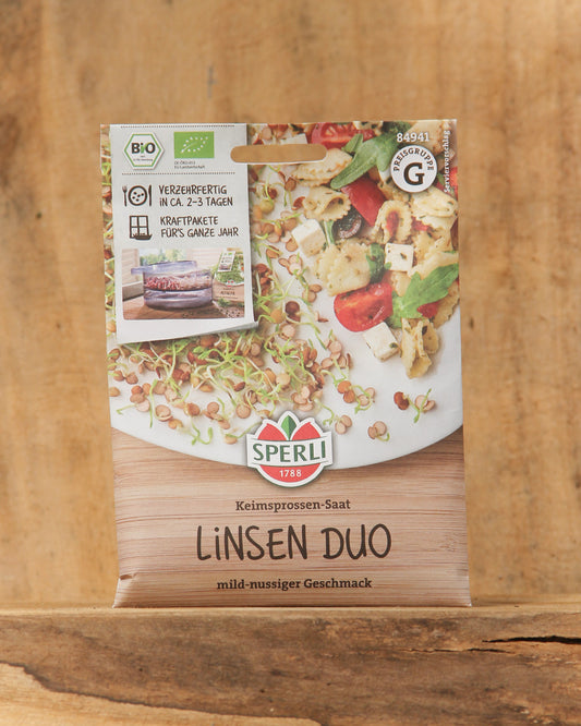 Eine Packung Sperli's | Bio Keimsprossen Saatgut 'Linsen Duo' von Sperli's mit Linsensprossen, dem Bio-Saatgut-Siegel und einem mild-nussigen Geschmack auf Deutsch liegt auf einer Holzfläche neben einem Linsengericht.