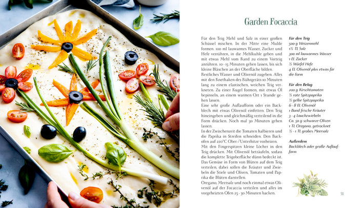 Eine Person verziert Focaccia-Teig mit buntem Gemüse und Kräutern und kreiert florale Muster, die von Naturillustrationen inspiriert sind, neben "Eine kleine Pause im Grünen | Kulinarische Vielfalt der Jahreszeiten" vom Hölker Verlag.