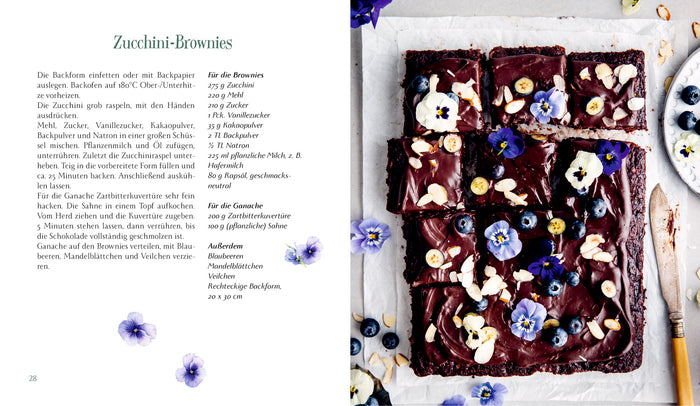 Ein Rezept aus "Eine kleine Pause im Grünen" vom Hölker Verlag zeigt auf der einen Seite eine deutsche Anleitung für Zucchini-Brownies, auf der anderen Seite ein Foto von Schokoladen-Brownies mit essbaren Blüten und Nüssen, die in Quadrate auf Weiß geschnitten sind.