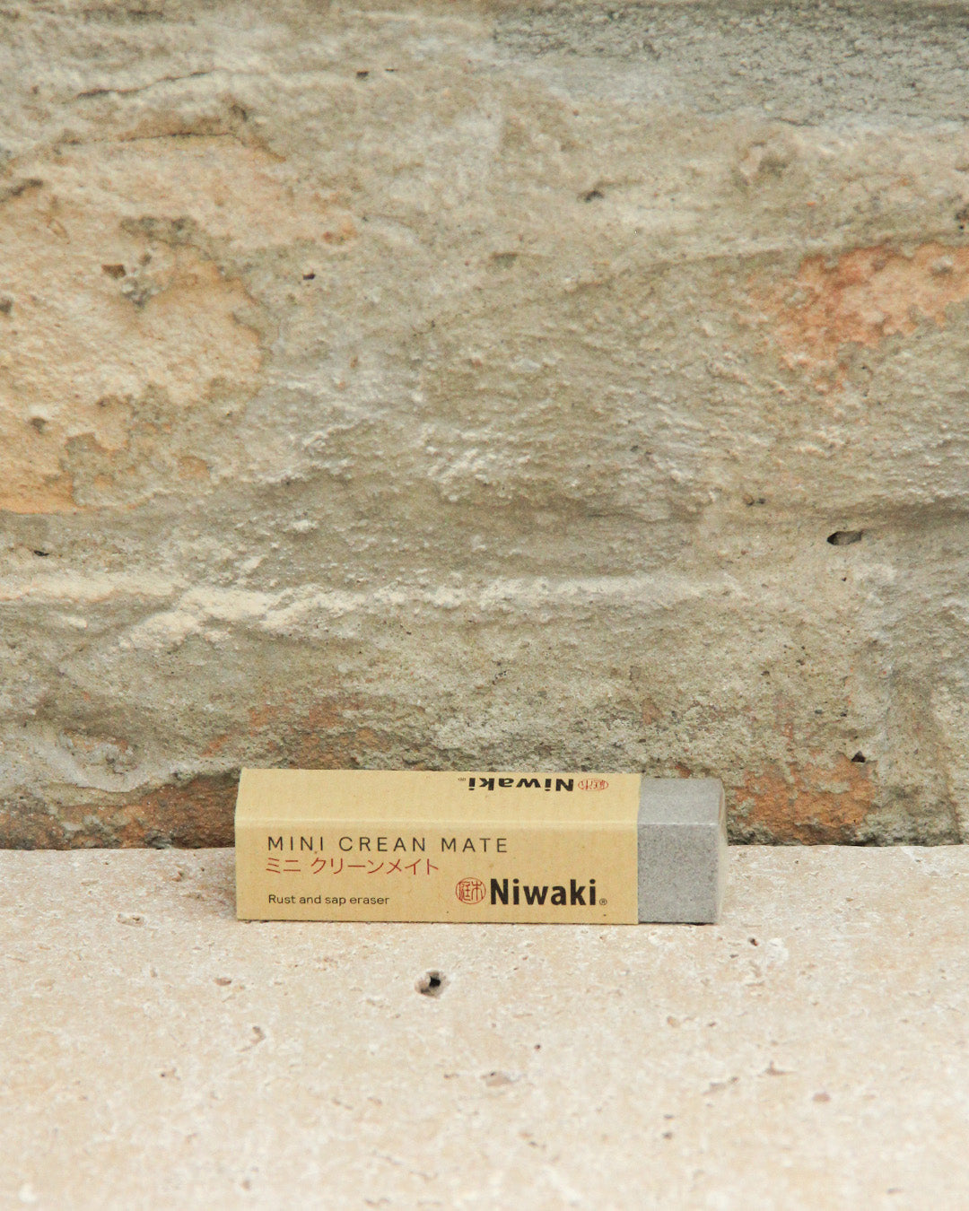 Der Niwaki | 'Mini Clean Mate' Rost- und Harzentferner ruht auf einer Steinfläche vor einer hellbraunen Steinwand, ideal zum Reinigen von Gartenwerkzeugen und Carbonstahl-Werkzeugen.