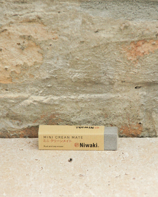 Der Niwaki | 'Mini Clean Mate' Rost- und Harzentferner ruht auf einer Steinfläche vor einer hellbraunen Steinwand, ideal zum Reinigen von Gartenwerkzeugen und Carbonstahl-Werkzeugen.