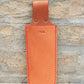 The Niwaki | „Saw Holster“ – eine hochwertige Lederschutzhülle für Klappsägen von Niwaki, gefertigt aus hellbraunem Leder mit roten Nähten und zwei Metallnieten, mit geprägten japanischen Schriftzeichen auf der Vorderseite, abgebildet vor dem Hintergrund einer Steinmauer.