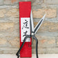 Niwaki | „Sentei Topiary Clippers“ – Buchsbaumschere in Schwarz, aufrecht vor einer strukturierten Backsteinmauer präsentiert, zusammen mit der markanten roten Schachtel mit japanischer Kalligraphie.