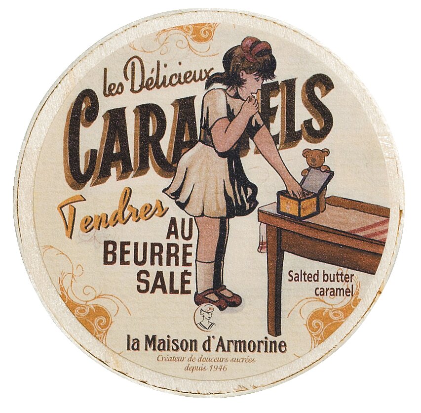 Rundes Etikett im Vintage-Stil mit einem Mädchen in Braun, das Karamell aus einer Schachtel nimmt. Text: Viani | Karamellbonbon mit gesalzener Butter 50 g, Gesalzenes Butterkaramell, plus dekorative Elemente und Markenname Viani.