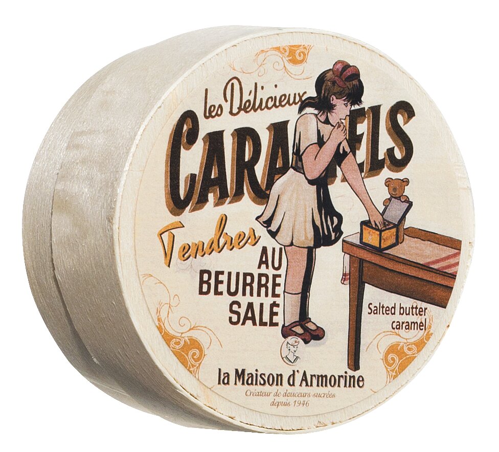 Runde Dose mit der Aufschrift Viani | Karamellbonbon mit gesalzener Butter 50 g, mit der Illustration eines Mädchens in einem Kleid, das auf einem Tisch nach Karamellbonbons greift; der Text enthält gesalzenes Butterkaramell und den Markennamen Viani.