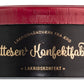 Eine schlichte, schwarz-rote Dose, verziert mit goldener Schrift und eleganten Details, zeigt das Markenlogo von „Hattesens Lakritzkonfekt“ sowie dänische Schriftzüge, darunter „Lakridshåndværk fra Ærø“ auf der Vorderseite, und bietet eine köstliche Auswahl an Lakritzkonfekt in einzigartigen Geschmacksrichtungen wie Blau-, Stachel- und Erdbeere.