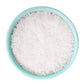 Eine türkisfarbene Schale, die an das ikonische „Keramiktopf“-Design erinnert, ist randvoll mit „Sal de Ibiza | ‚Fleur de Sel‘ Meersalz 150 g“ – das grobkörnige weiße Meersalz, von oben betrachtet vor einem makellos weißen Hintergrund, verkörpert die handwerkliche Essenz von Sal de Ibiza.