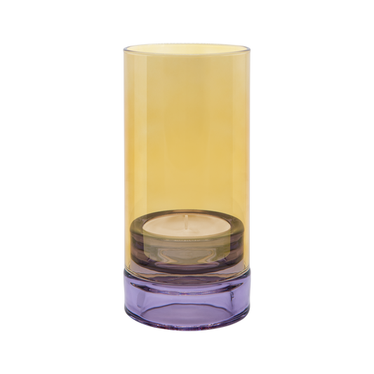 Das „Remember | Windlicht ‚Lys‘“ in Flieder von Remember ist ein zylindrischer Kerzenhalter aus Glas mit einem gelben Oberteil und einem violetten Sockel, in dem eine kleine Teelichtkerze steckt.